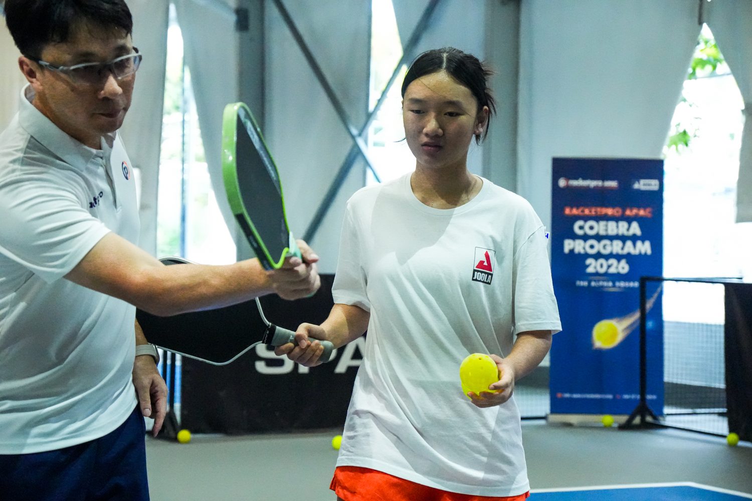 Coach Mark Teo guiding a junior player's paddle grip in a one-on-one pickleball lesson