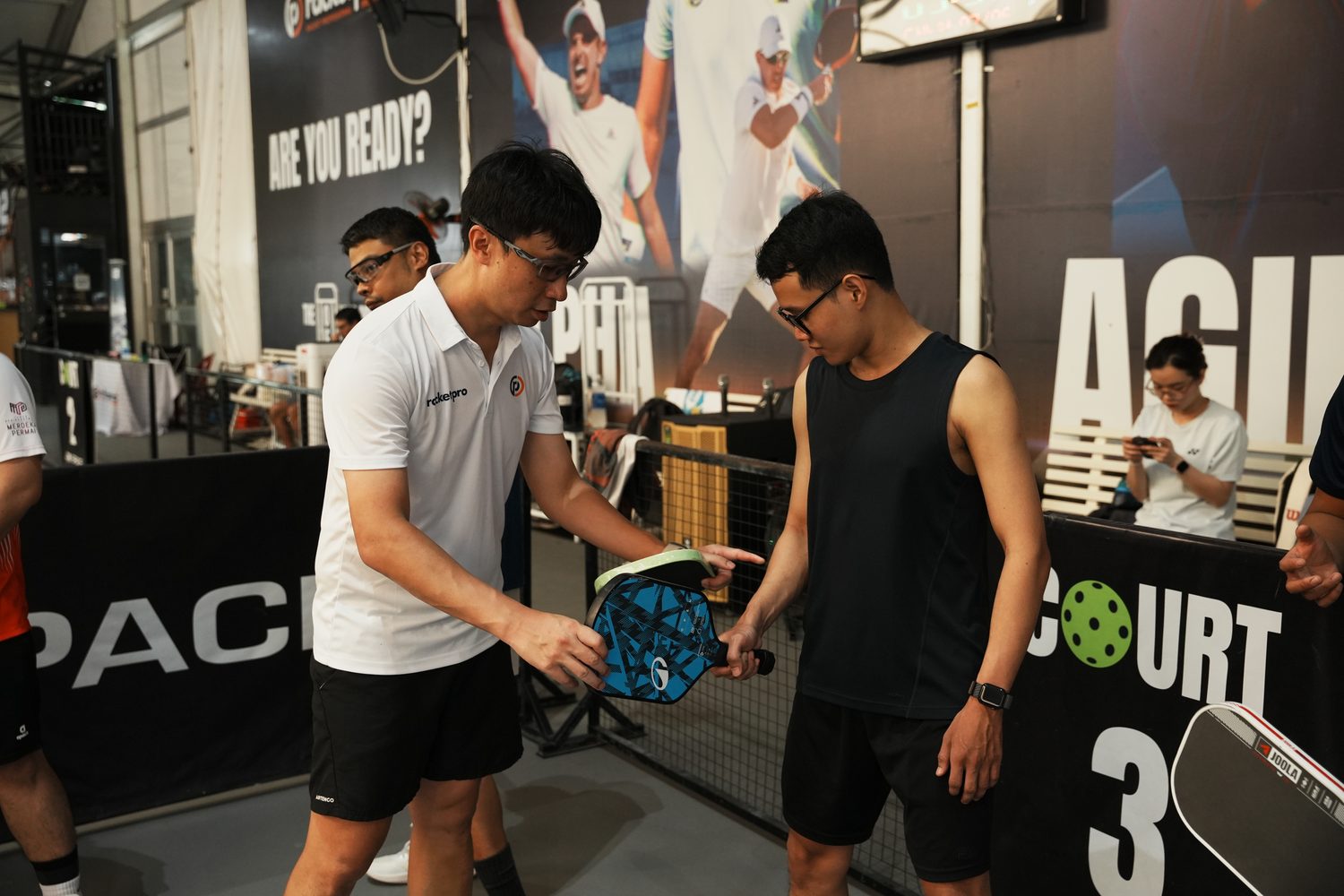 Pickleball coach Mark Teo demonstrating paddle selection to a player at a coaching event